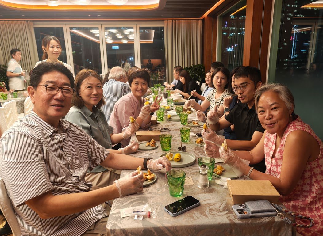 Members in gloves at a long table set with durian and green glasses