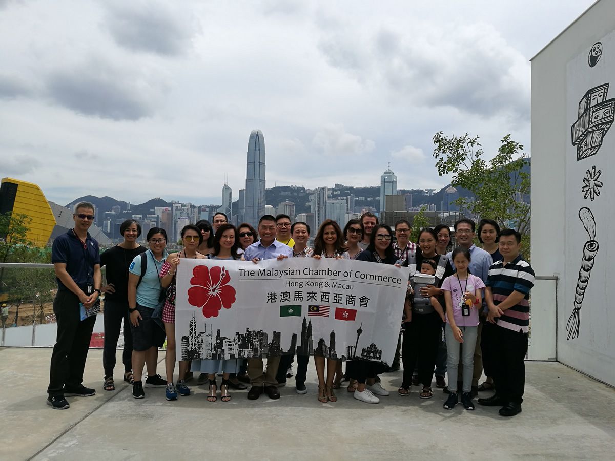 Members with the MAYCHAM banner on a terrace, the Hong Kong Island skyline across the harbour behind them