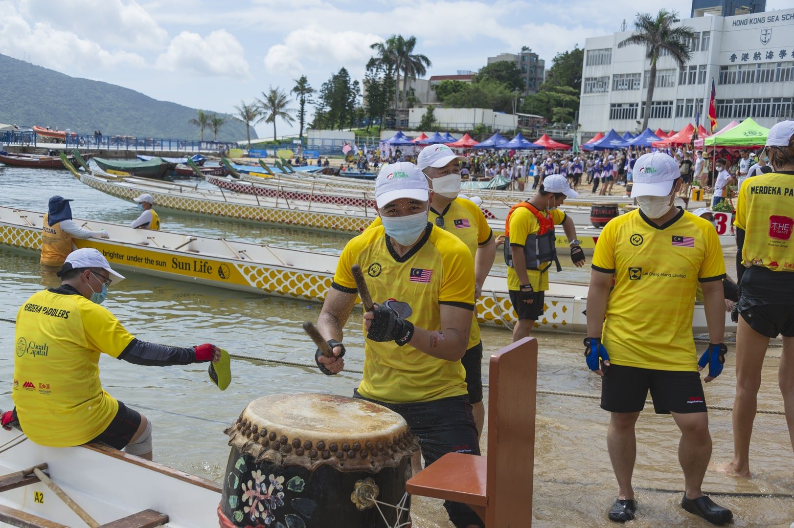 Merdeka Paddlers in yellow team shirts at the drum beside the dragon boats on the beach at Stanley